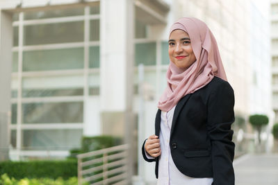 Portrait of smiling businesswoman wearing hijab while standing against building