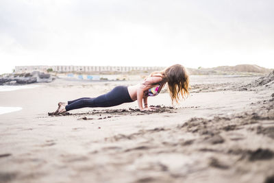 Side view of woman exercising at beach against sky