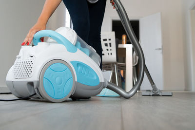 Midsection of woman cleaning floor with vacuum cleaner while standing at home