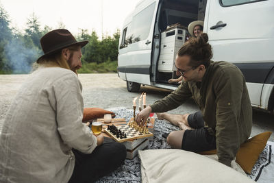 Male friends playing chess while spending leisure time by motor home