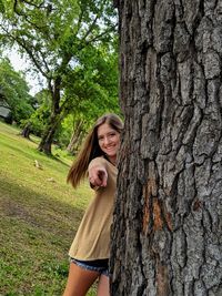 Portrait of smiling young woman against tree trunk