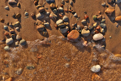 Directly above flatlay of gentle waves lapping sand and pebble beach with pristine clear cool water