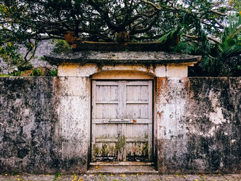 Closed door on abandoned surrounding wall against trees