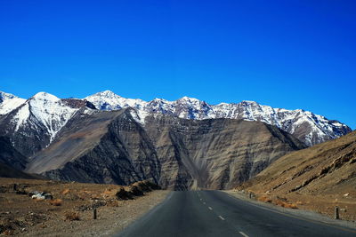 Road amidst snowcapped mountains against clear blue sky