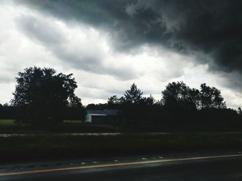 Trees on landscape against cloudy sky