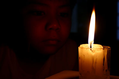 Close-up of boy looking at lit candle in darkroom