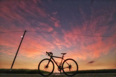 Silhouette bicycle on field against sky during sunset