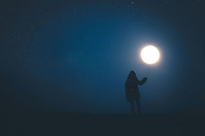 Optical illusion of woman holding moon at night