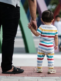 Low section of man and his toddler son walking on the street