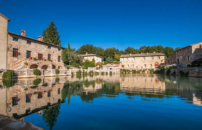 Reflection of buildings in lake against clear blue sky, bagno vigoni, italy