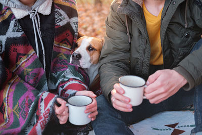 Midsection of couple holding coffee cup sitting with dog outdoors