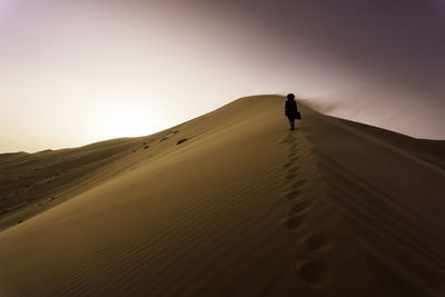 Man standing on sand dune in desert against clear sky