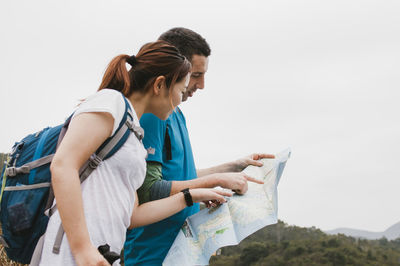 Friends analyzing map while standing against clear sky