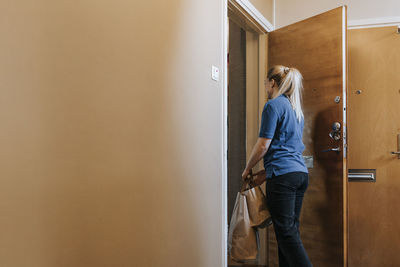 Female caregiver holding bags while standing near door at home