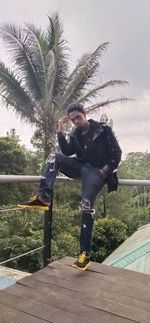 Young man standing by palm tree against sky