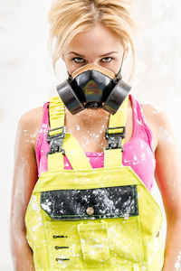 Portrait of female construction worker wearing protective mask against wall