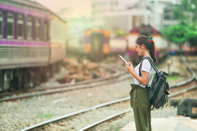 Side view of man using mobile phone while standing on railroad track