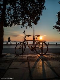 Silhouette people riding bicycle on street against sky at sunset