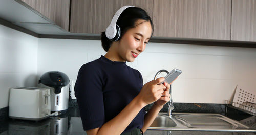 Woman using mobile phone while listening music at home