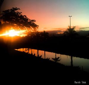 Silhouette trees by lake against sky during sunset