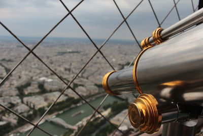 Close-up of metal fence by city skyline against sky