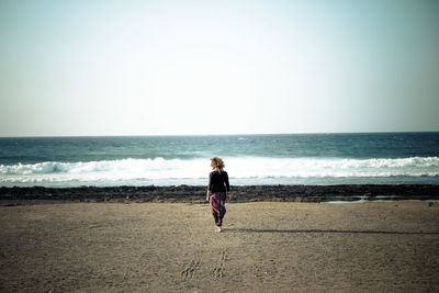 Rear view of woman at shore of beach against sky