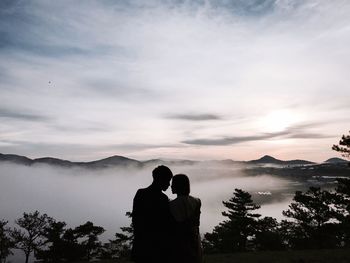 Silhouette couple standing on mountain against cloudy sky