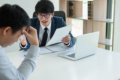 Businessman gesturing at colleague while sitting at desk