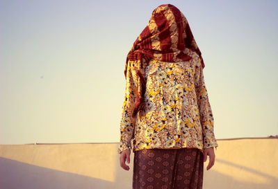 Woman with covered face standing against sky