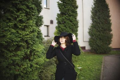 Portrait of woman holding hat while standing against trees