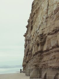 People on rock formation by sea against sky