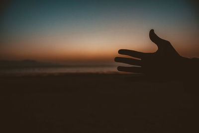 Close-up of silhouette hand against sea during sunset