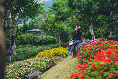 Woman amidst flowering plants sitting on rock against trees