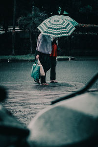 Full length of man holding umbrella walking in rainy season