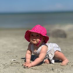 Baby girl in a pink summer hat crawling on a beach and smiling 