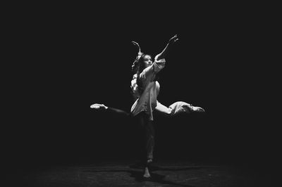 Full length of woman dancing against black background