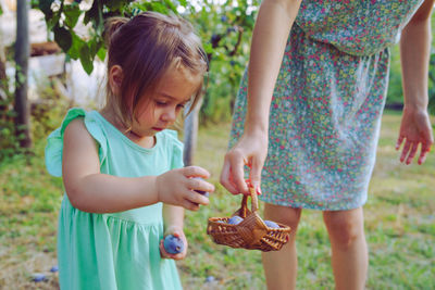 Woman holding easter eggs in basket by daughter standing on grass