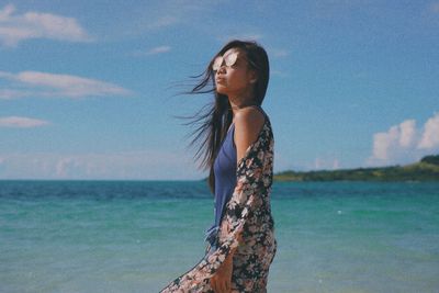 Side view of young woman standing in sea against sky