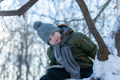 Portrait of woman sitting on tree during winter