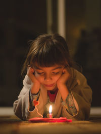 Close-up of girl blowing candle while lying on floor in darkroom