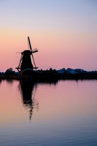 Traditional windmill by lake against sky during sunset