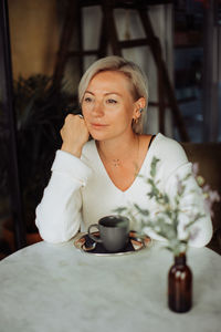 Blond stylish woman sitting alone at table with cup of coffee