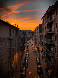 Vehicles on street amidst buildings against sky during sunset