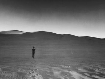 Rear view of man walking at desert against clear sky