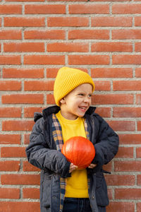 Boy with a pumpkin in his hands against a brick wall.