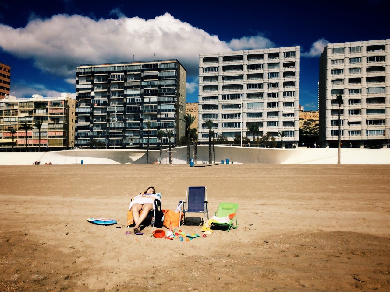 building exterior, architecture, built structure, sky, men, full length, city, cloud - sky, sand, sitting, lifestyles, day, rear view, beach, leisure activity, chair, relaxation, outdoors