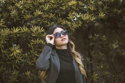 Young woman wearing sunglasses standing by plants