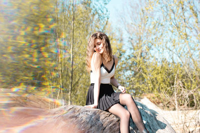Beautiful young woman sitting on rock against trees in forest
