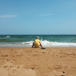 Rear view of man sitting on beach against sky