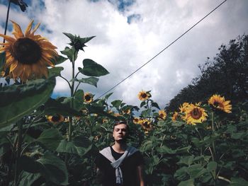 Man standing in sunflower field against cloudy sky
